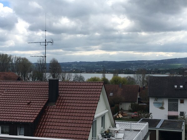 A residential area with red-tiled roofs, a view of a lake, and a cloudy sky.