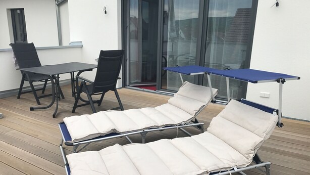 A sunbed with a canopy, a table, and two chairs on a wooden deck. - High quality 1 1/2 room apt. with lake view and large terrace! (Allensbach)