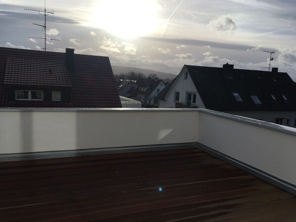 A rooftop terrace with a wooden floor, white walls, and multiple antennas.