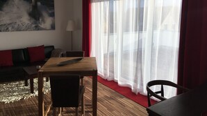 A room with a wooden table, a sofa, a chair, and a large window with sheer curtains. - High quality 1 1/2 room apt. with lake view and large terrace! (Allensbach)