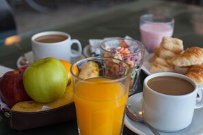 Ein Frühstücksbuffet mit verschiedenen Speisen, darunter Obst, ein Glas Orangensaft und zwei Tassen Kaffee.