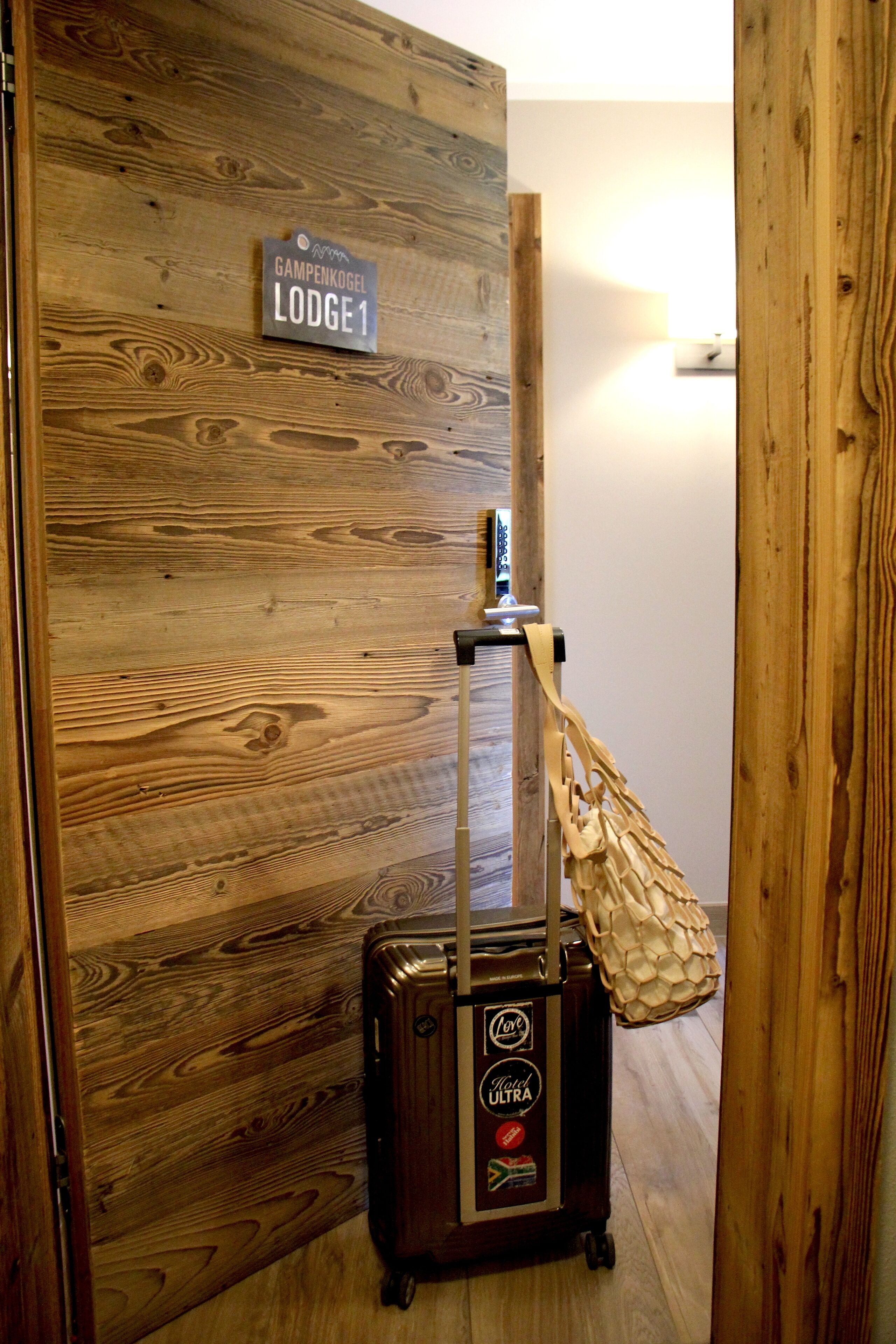 A wooden wall with a sign reading "Gampenkogel Lodge 1" and a suitcase with a "Cool Ultra" sticker.