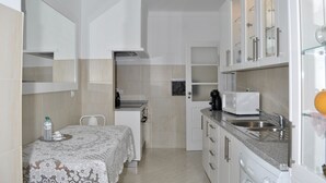Une cuisine compacte avec des meubles blancs, un four à micro-ondes, un évier et un coin repas avec une table dressée pour deux personnes.
