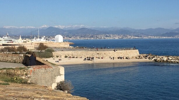 Une zone côtière avec un mur de pierre, une plage et une vue lointaine sur la ville.