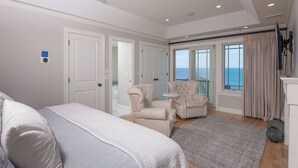 Una camera da letto con un letto grande, due poltrone, un tavolino e vista mare da un balcone.