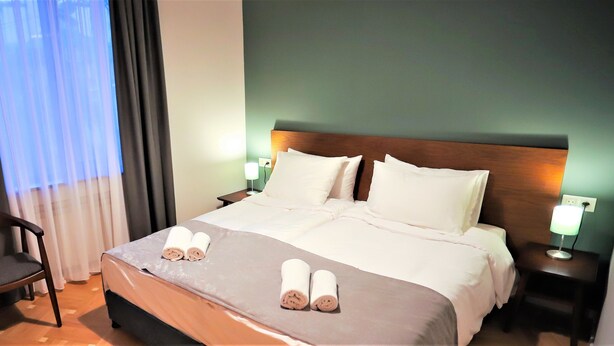 Una habitación de hotel con una cama bien hecha, dos lámparas de noche, una silla y una ventana con cortinas.