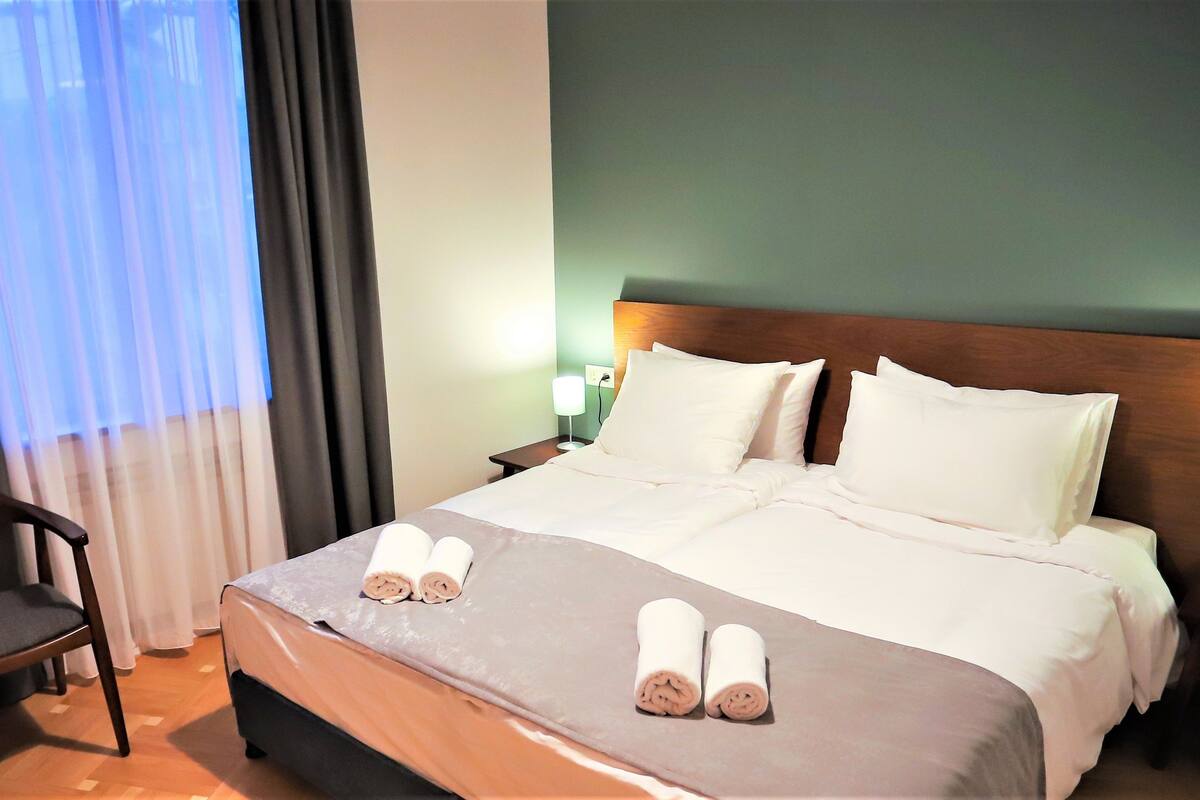 Una habitación de hotel con una cama bien hecha, dos lámparas de noche, una silla y una ventana con cortinas.
