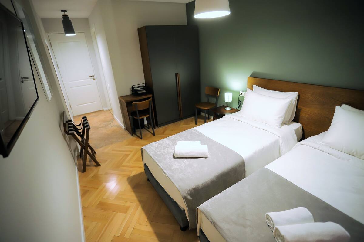 Habitación de hotel con dos camas, un escritorio, una silla y una lámpara.