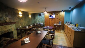 Un restaurante con mesas y sillas de madera, un muro de piedra y una pantalla de televisión.