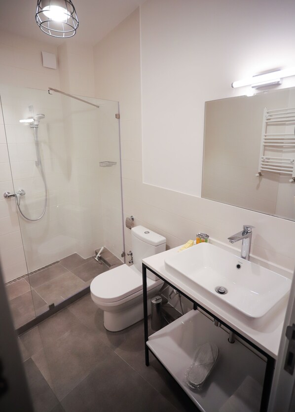 A modern bathroom with a glass shower enclosure, a white toilet, and a white sink with a mirror above it. - Hotel Sabu (Tbilisi)