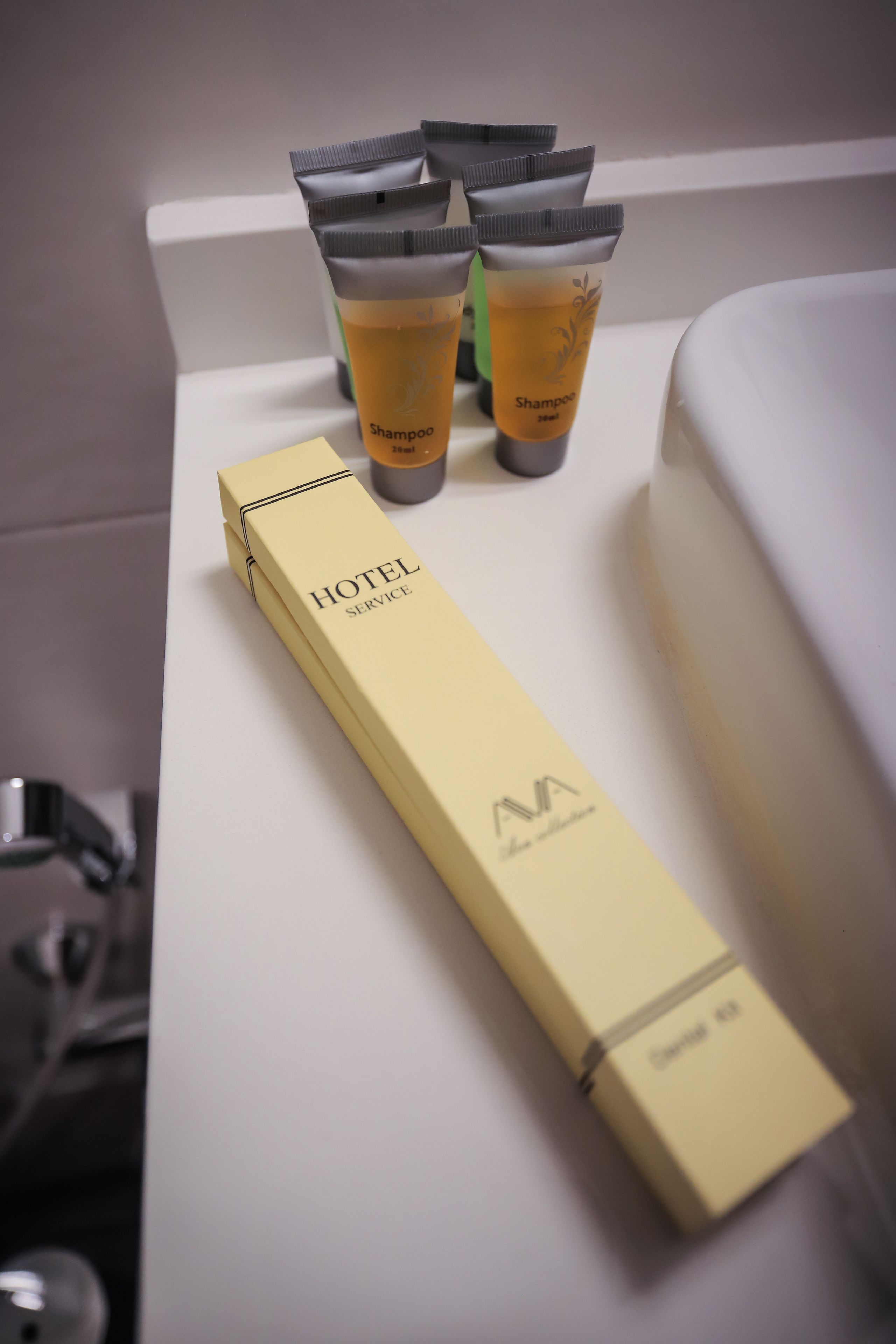 En hotellåda med hygienartiklar och små tuber med schampo på en hylla i badrummet.