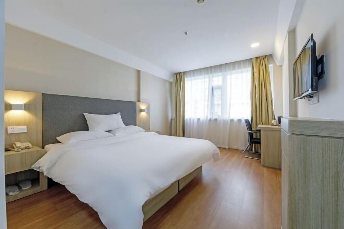A hotel room with a large bed, bedside tables, a desk, and a TV mounted on the wall.