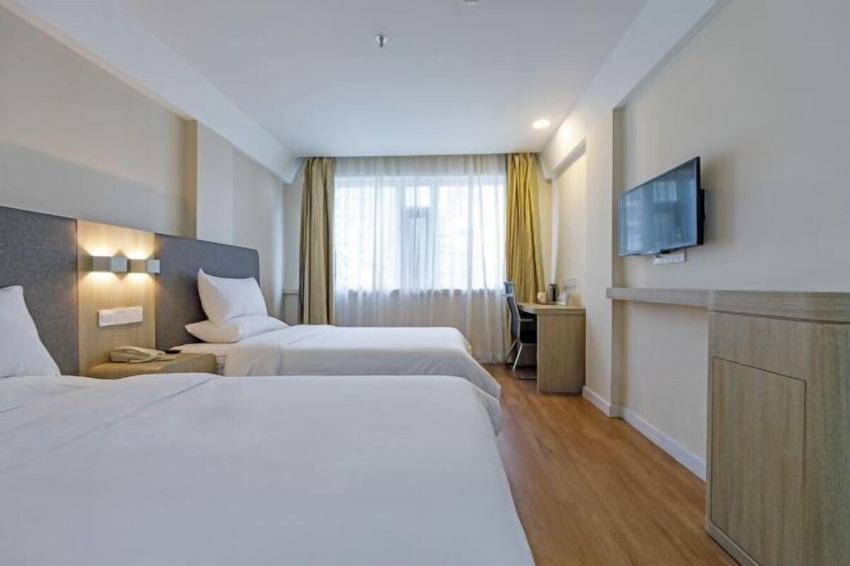 A hotel room with two beds, a desk, a chair, a television, and a window with curtains.