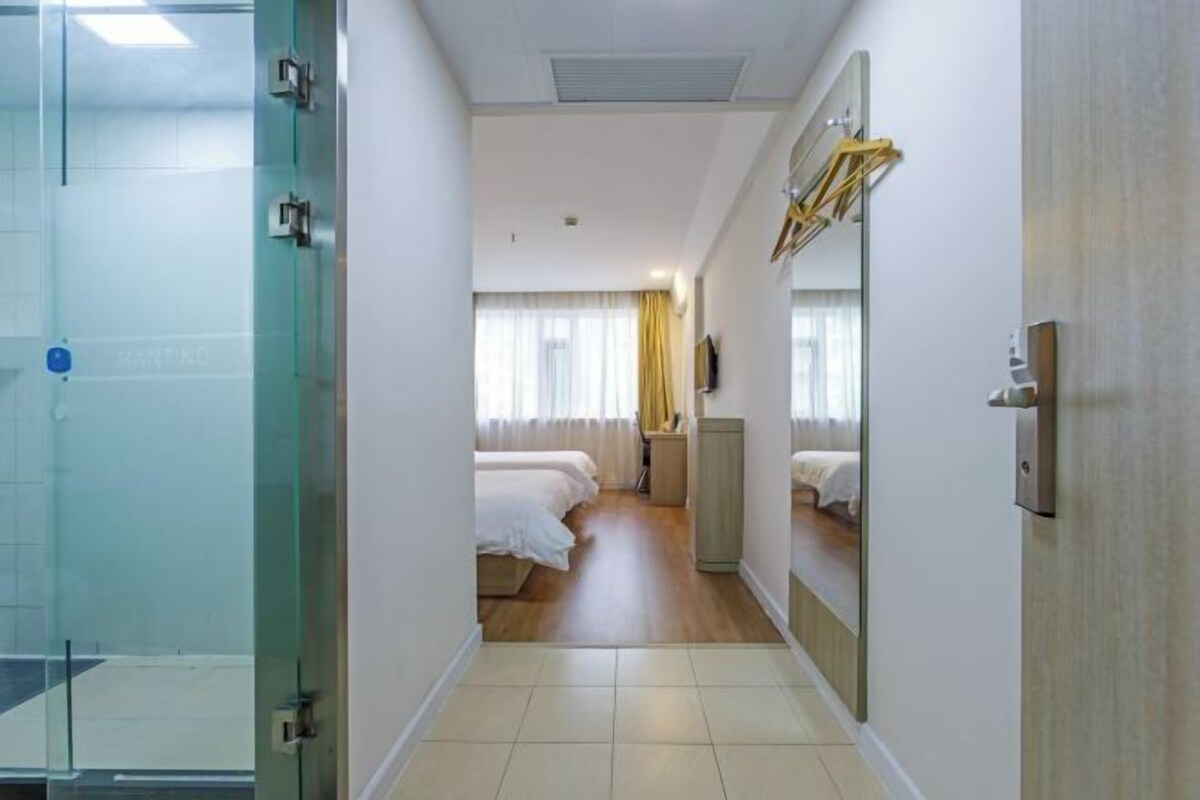 A hotel room with a glass shower enclosure, a bed with white linens, a bedside table, a mirror, and a wardrobe.