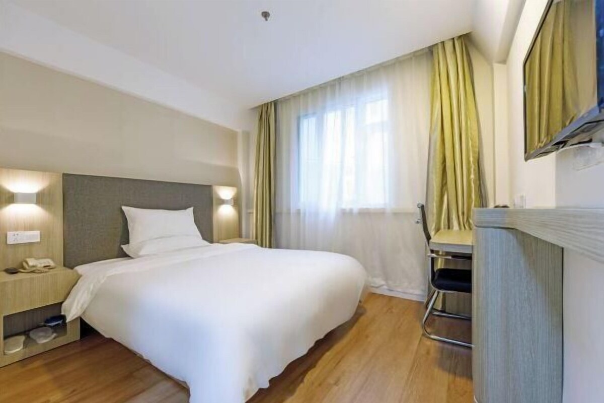 A hotel room with a bed, bedside table, lamp, and a desk with a chair.
