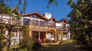 A two-story building with a balcony, a covered patio, and a well-maintained garden. - Shemak Posada (Villa General Belgrano)