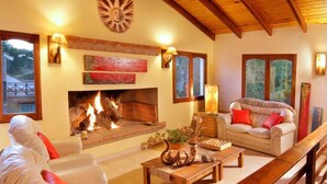 A cozy living room with a fireplace, a sofa, a coffee table, and a wooden ceiling. - Shemak Posada (Villa General Belgrano)