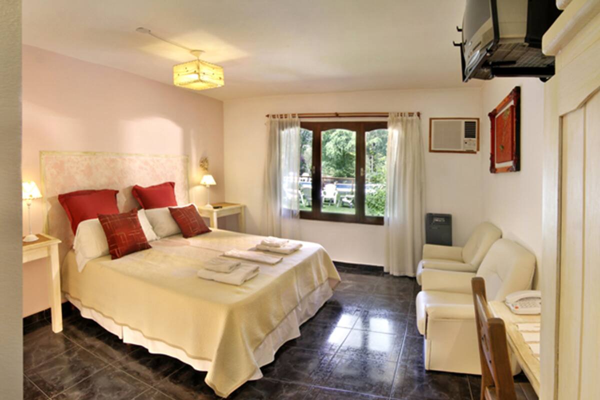 A bedroom with a large bed, two bedside tables, a nightstand, a window with curtains, a chair, and a television.