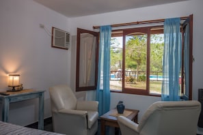 Une pièce avec deux chaises, une petite table, une lampe et une fenêtre avec des rideaux.