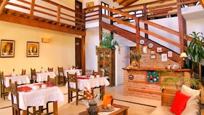 A spacious dining area with multiple tables and chairs, a fireplace, and a staircase. - Shemak Posada (Villa General Belgrano)