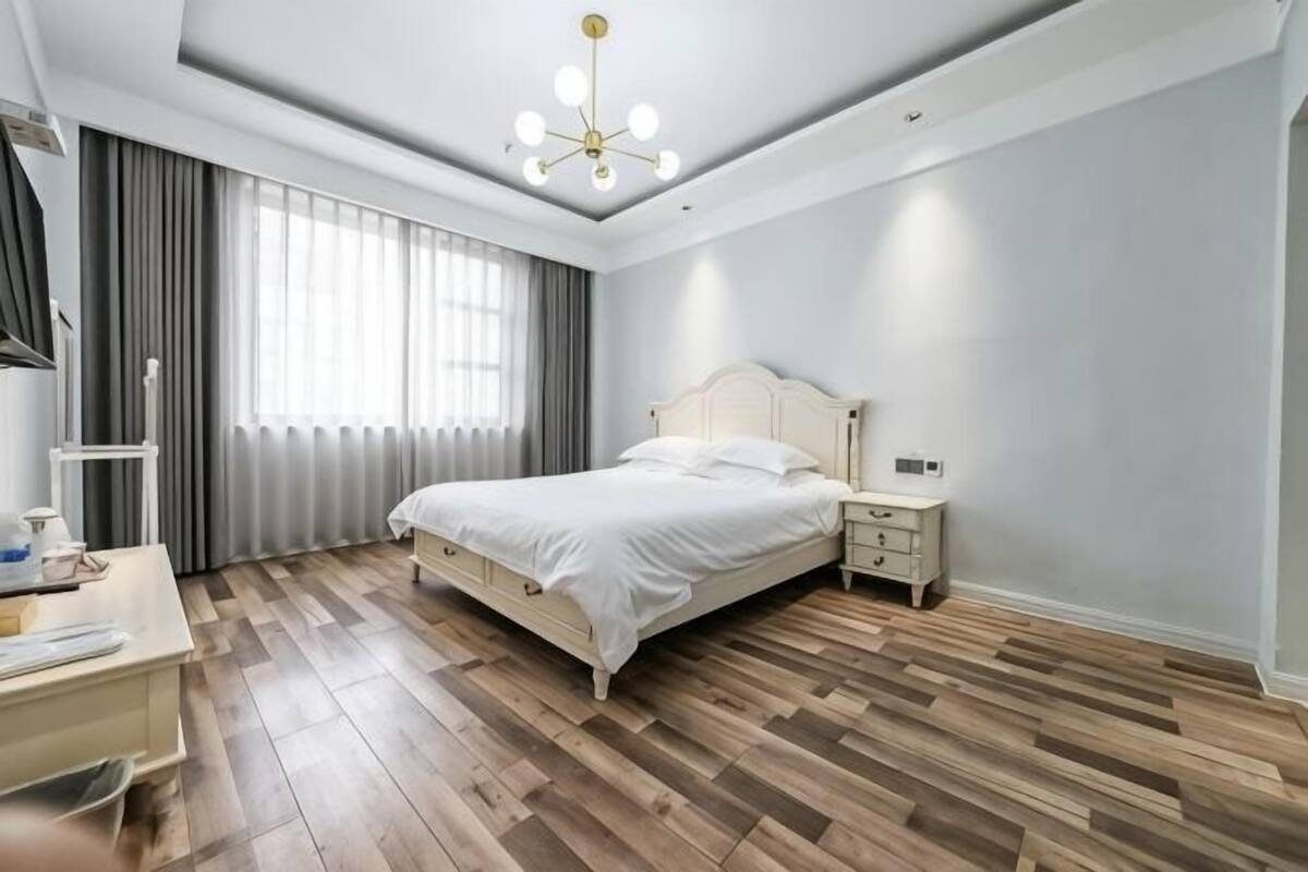 Een slaapkamer met een bed, nachtkastjes, een bureau en een raam met gordijnen.