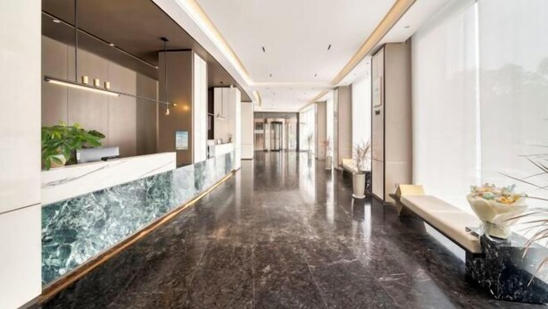 Um hall de hotel moderno com um balcão de recepção de mármore, áreas de estar e grandes janelas.