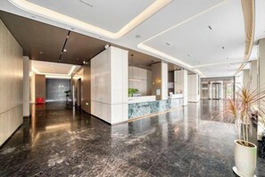 A modern hotel lobby with a marble floor, a reception desk, and a plant.