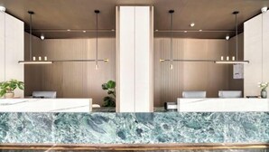 Uma área de recepção com bancadas de mármore, dois balcões de atendimento, iluminação pendente e um pilar vertical.