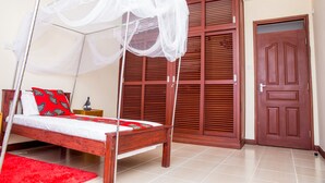 A bedroom with a wooden bed, a red rug, a white canopy bed, and a wooden wardrobe. - Safiri Kenya Home (Mombasa)