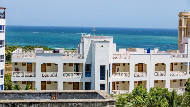 A white building with multiple balconies overlooking a clear blue sea. - Safiri Kenya Home (Mombasa)