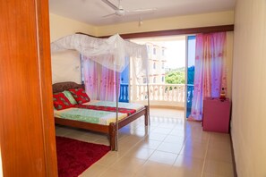 A bedroom with a bed, a red rug, a balcony with curtains, and a ceiling fan.