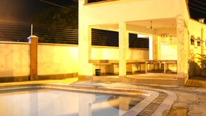 A swimming pool area with a covered seating area and a building with a signboard. - Safiri Kenya Home (Mombasa)