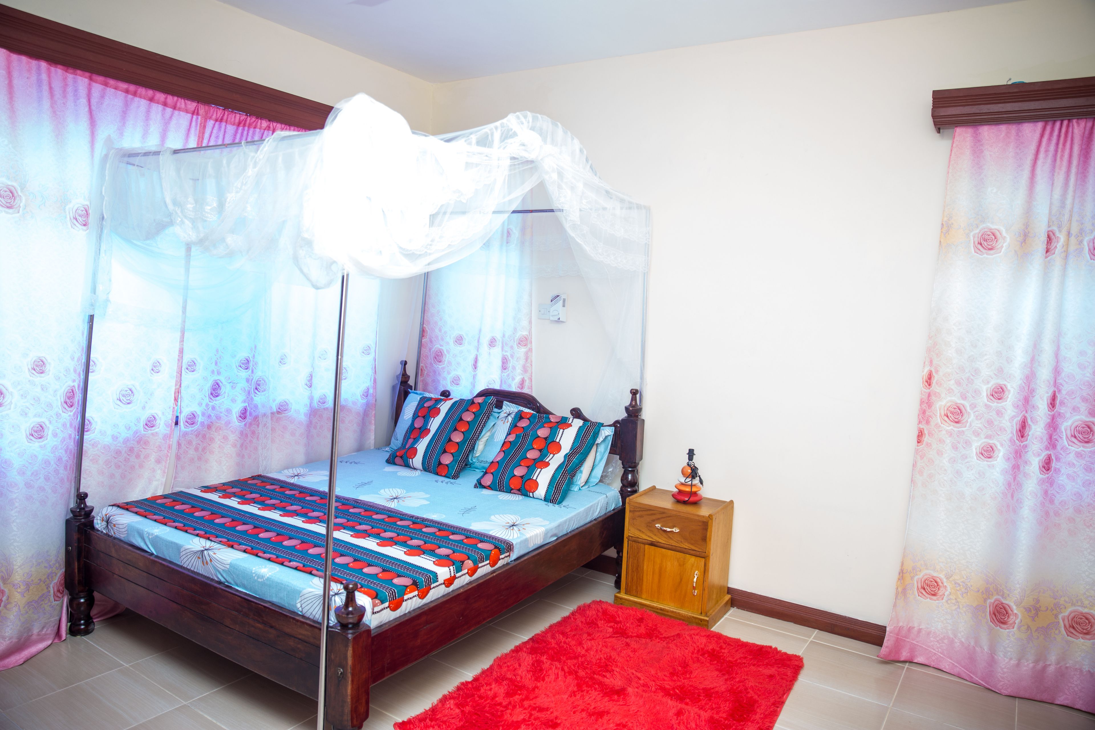 Un dormitorio con una cama con dosel, una mesita de noche de madera y una alfombra roja.