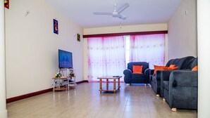 A living room with a TV, a sofa, a coffee table, and a ceiling fan. - Safiri Kenya Home (Mombasa)