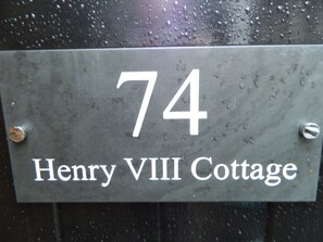 A metal house number sign with "74" and "Henry VIII Cottage" written on it.