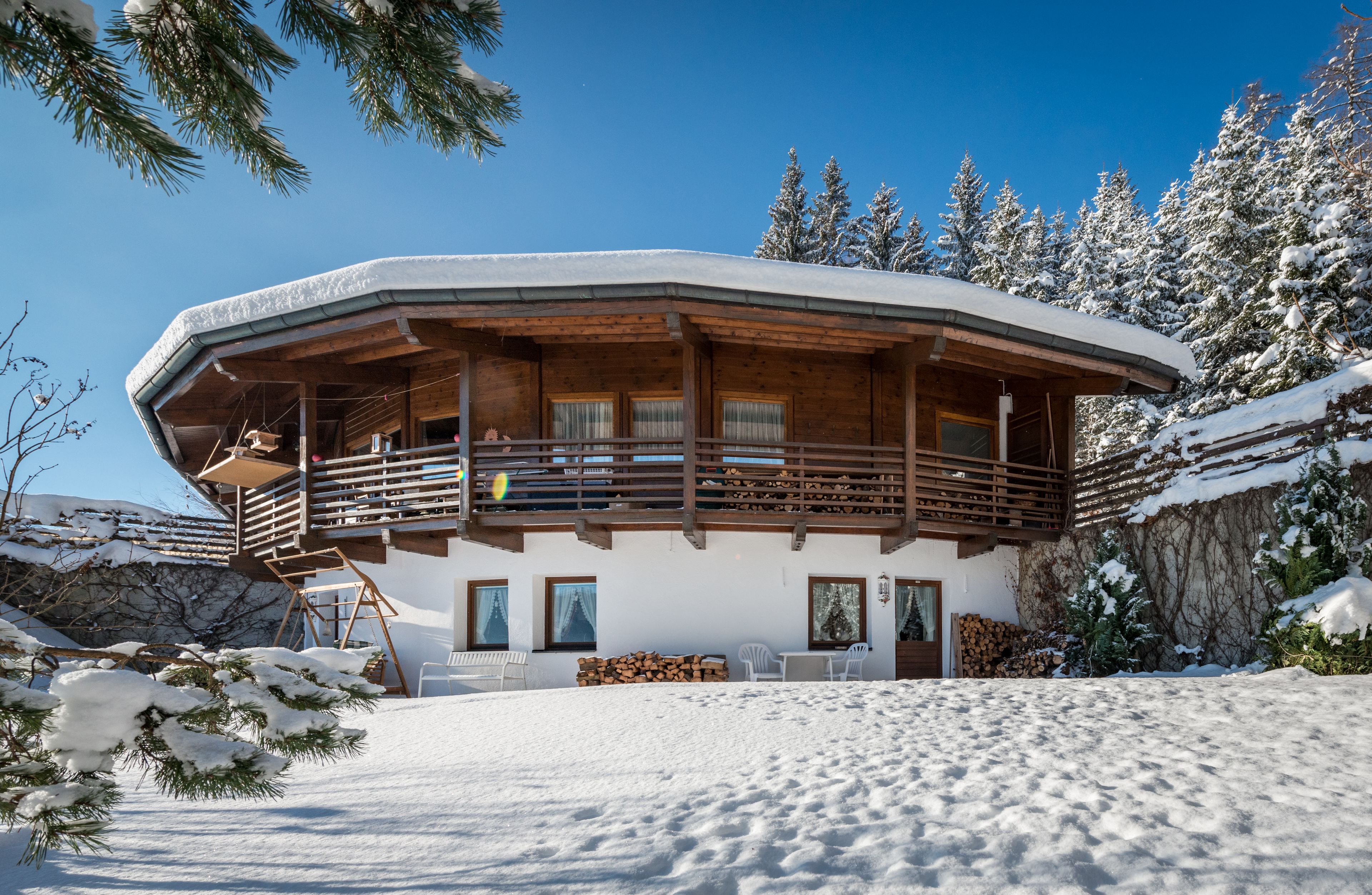 Una cabaña de madera con balcón, rodeada de árboles cubiertos de nieve y un cielo despejado.