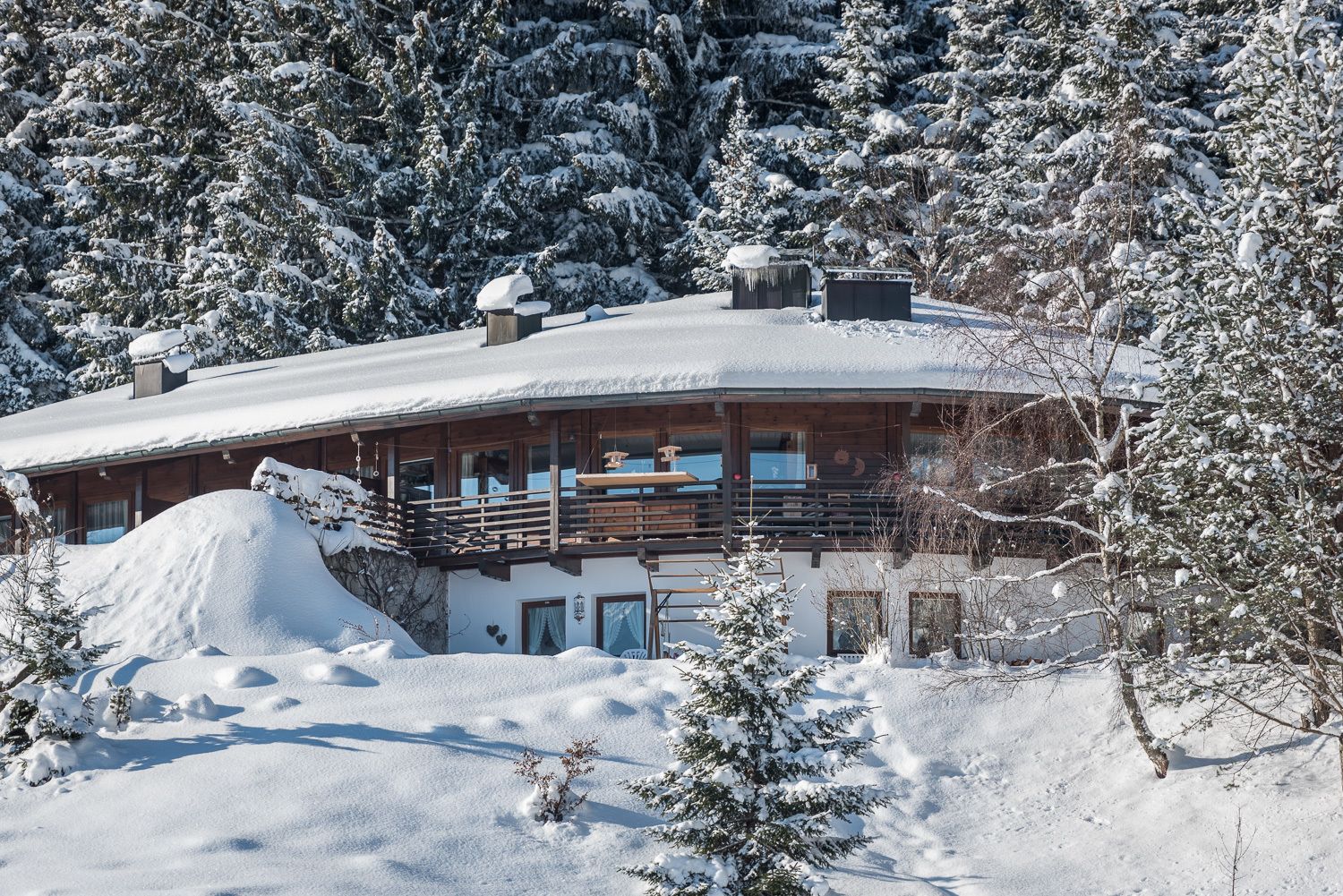 Un chalet enneigé, avec une façade en bois, un balcon et une grande pile de neige devant.