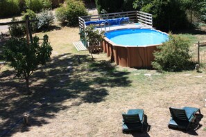 Un patio trasero con piscina, terraza de madera y dos sillones de descanso.