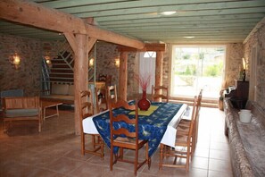 Un comedor rústico con una mesa y sillas de madera, un muro de piedra y una escalera al fondo.