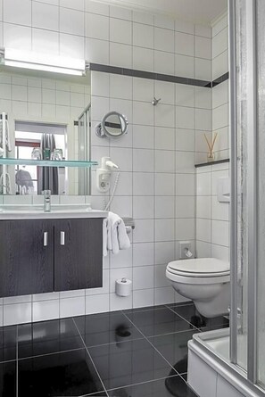 Une salle de bain moderne avec un meuble-lavabo en bois foncé, une étagère en verre, des toilettes blanches et une cabine de douche en verre.