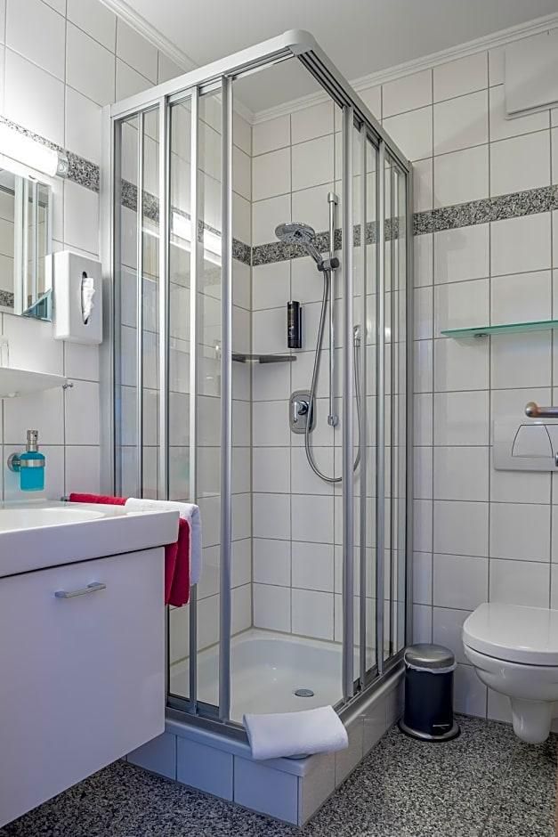 Ein modernes Badezimmer mit einer gläsernen Duschkabine, einem weißen Waschbecken und einem roten Handtuch sowie einer weißen Toilette.