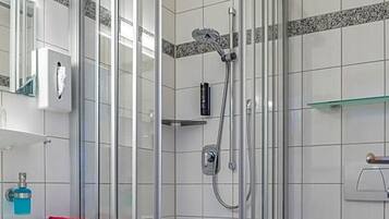 Ein modernes Badezimmer mit einer gläsernen Duschkabine, einem weißen Waschbecken und einem roten Handtuch sowie einer weißen Toilette.