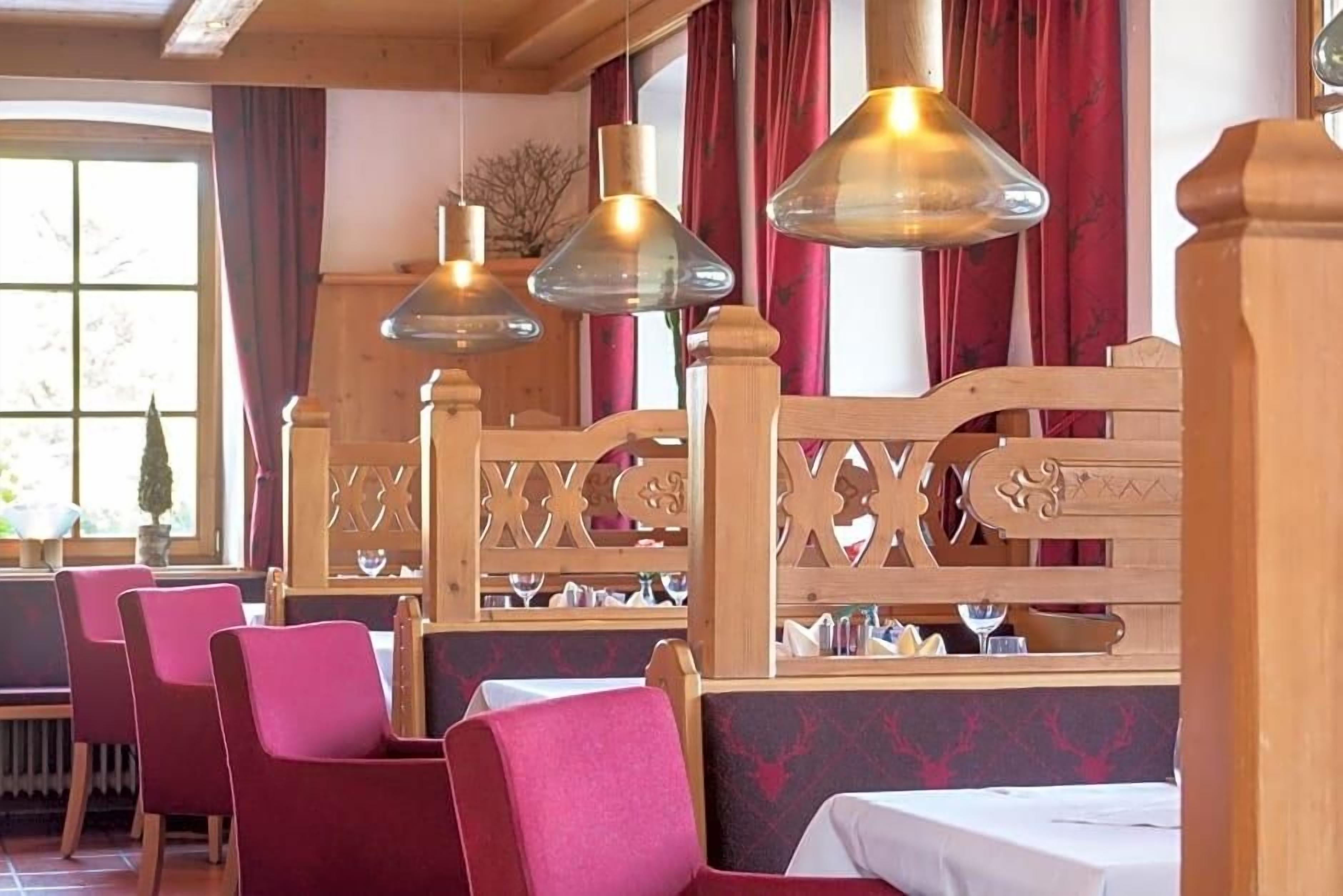 Een restaurantinterieur met houten zithoekjes, rode bekleden stoelen en hangende lampen.