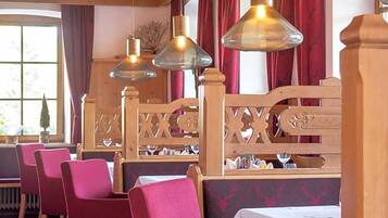 Een restaurantinterieur met houten zithoekjes, rode bekleden stoelen en hangende lampen.