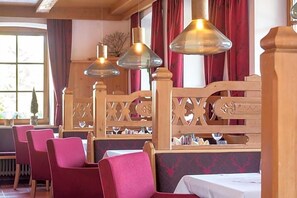 A restaurant interior with wooden booths, red upholstered chairs, and hanging pendant lights.
