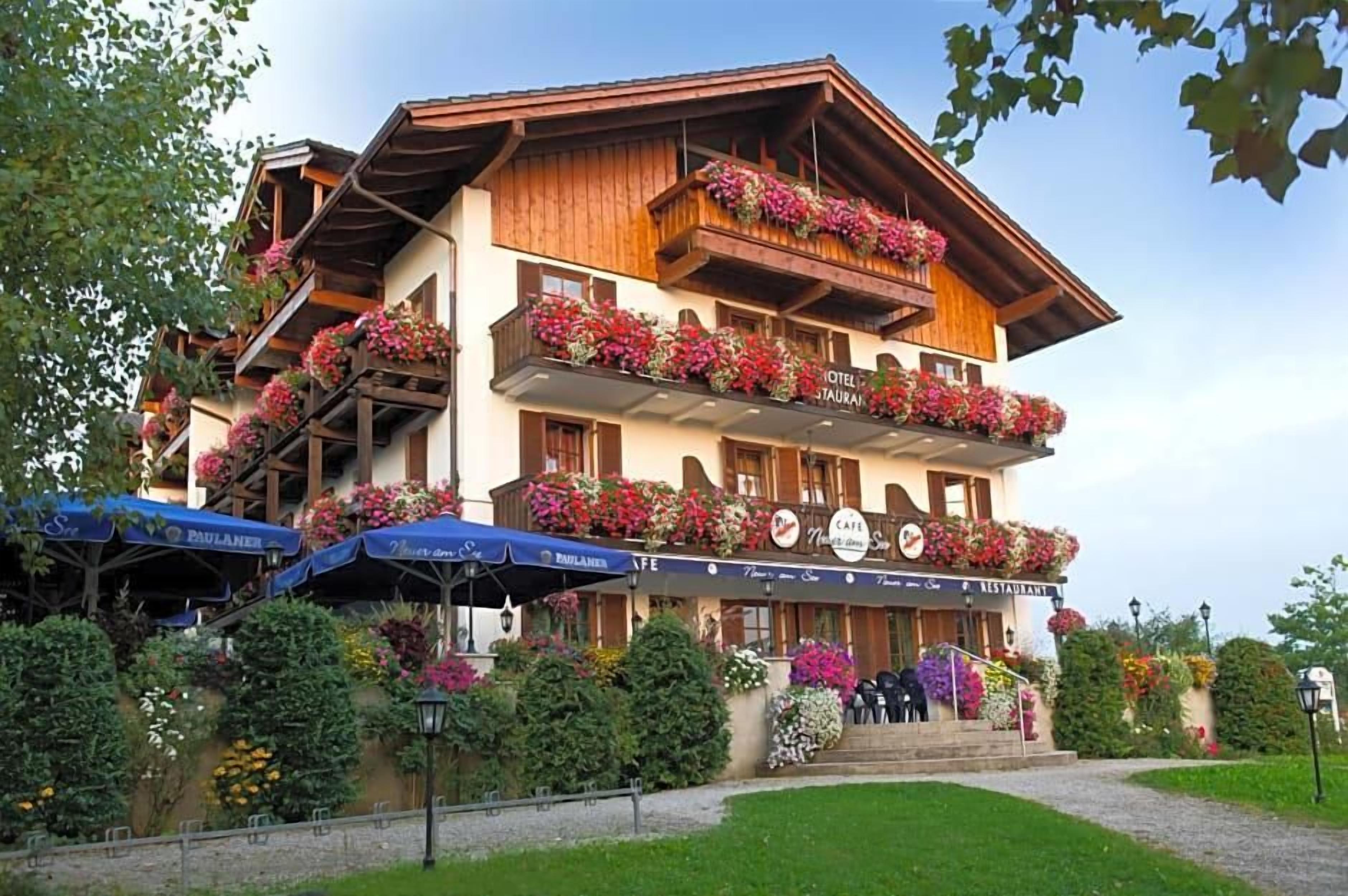Un immeuble à plusieurs étages, doté de balcons ornés de fleurs, d’une enseigne indiquant un restaurant et d’une terrasse avec des parasols.