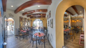 Interior de restaurante con vigas de madera, mesas con manteles individuales rojos y una pared de ladrillo.