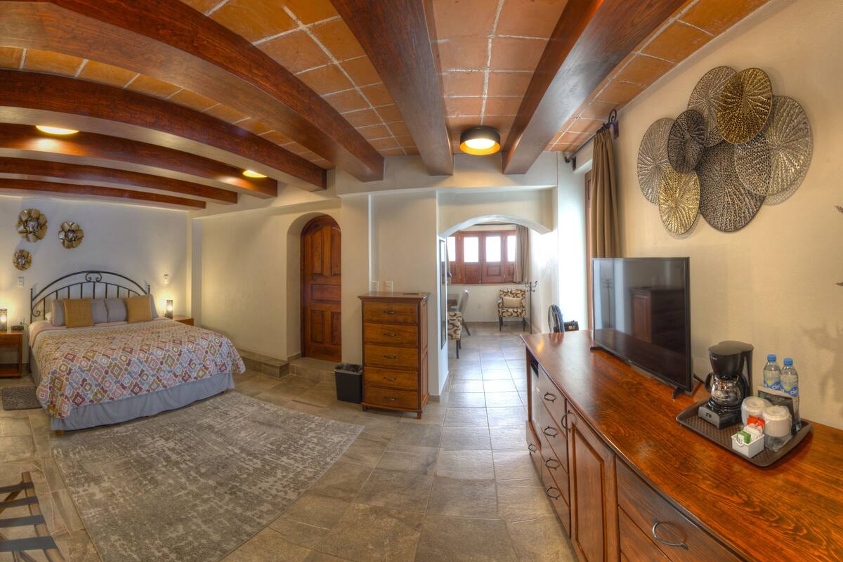 A bedroom with a bed, wooden dresser, and a TV on a wooden cabinet.