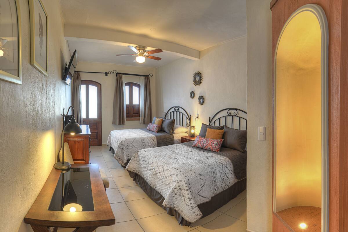 A bedroom with two beds, a desk, a ceiling fan, and a mirror.