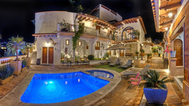 Una casa de dos pisos con piscina, mobiliario exterior y balcón.